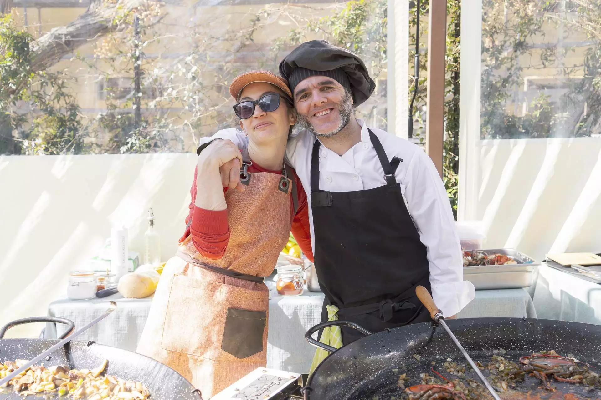 Una cocinera y un cocinero posan abrazados mientras cocinan una paella